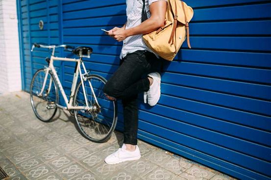 A tall guy with a phone and a bicycle standing next to a blue wall